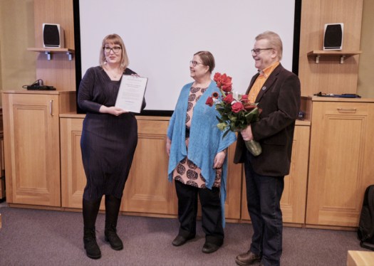 Henna stands with the award plaque and a boquet of flowers, Liisa and Arto stand beside her and smile.