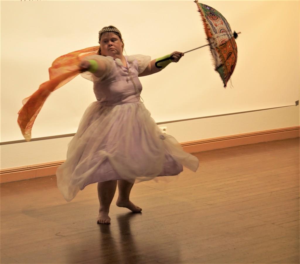 Hanna Rajapolvi vaaleanpunaisessa mekossa tanssimassa huivin ja auringonvarjon kanssa.